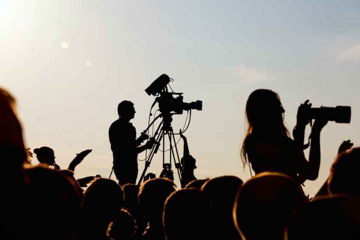 Silhouette au coucher du soleil d'un caméraman et photographe prenant des photos d'un concert de la foule